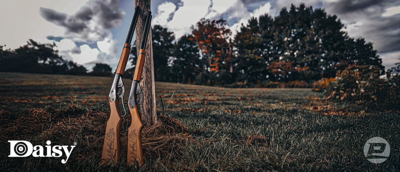 The Daisy Red Ryder bb guns both youth and adult leaning on a tree